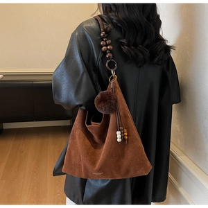 Détail du cabas en daim marron avec bandoulière en perles de bois et pompons sur modèle
