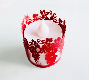 Macro shot of red laser-cut vine pattern paper sleeve on an LED flameless candle light