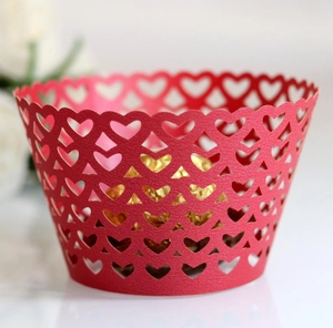 Macro detail of laser-cut red paper cupcake wrapper with heart patterns and gold chocolate