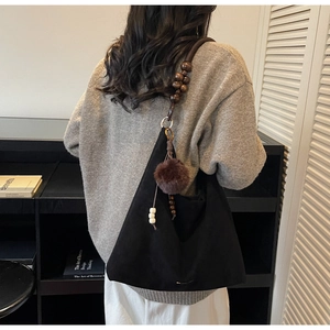 Détail du sac hobo en daim noir avec bandoulière en perles de bois et pompon en peluche