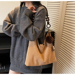 Detail of warm camel suede tote bag with wooden bead strap and plush tassel charm