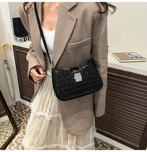 Detail of black baguette bag featuring woven texture and silver metal buckle on strap