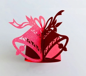 Macro detail of laser-cut 3D Christmas bell napkin ring with red and pink glitter finish