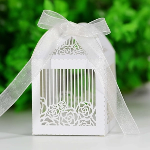 Close-up of white laser-cut birdcage wedding favor box with rose details and ribbon