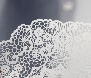 Detail of laser-cut white lace invitation card with intricate floral pattern texture