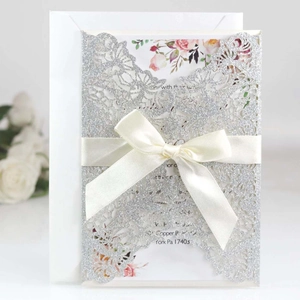 Detailed laser-cut silver glitter invitation featuring a cream ribbon bow and floral insert