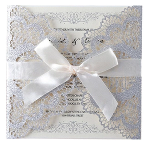 Detail of silver glitter laser-cut wedding invitation with ivory card and white silk bow