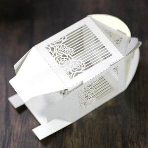 Macro shot of laser-cut white pearl paper candy box with rose hollow floral patterns