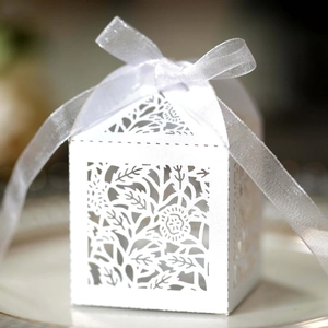 Macro shot of white laser-cut wedding candy box with floral patterns and a ribbon bow