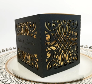 Elegant laser-cut hollow black wedding favor box with gold interior on white porcelain plate