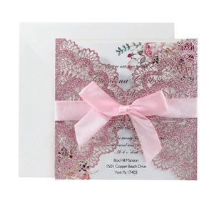 Detailed laser-cut glitter wedding invitation with pink ribbon bow and floral insert