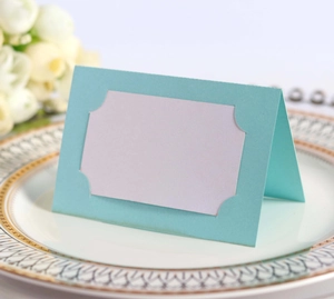 Détail d'un marque-place de mariage bleu ajouré posé sur une assiette à bordure dorée