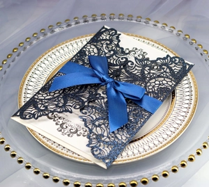 Detail of laser-cut navy blue wedding invitation with silk ribbon bow and vintage patterns