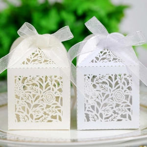 Close-up of laser-cut ivory floral favor boxes with delicate organza ribbon bows