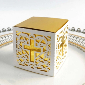 Detail showing white and gold laser-cut cross favor box on an elegant white ceramic plate