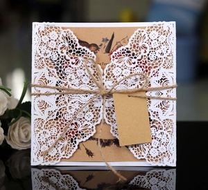 Detail of laser-cut lace wedding invitation with kraft paper, twine and floral motifs