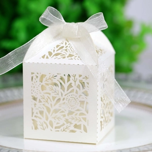 Close-up of laser-cut white favor box with elegant floral patterns and a ribbon bow
