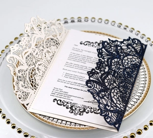 Detail of laser-cut rose gold and navy blue wedding invitations on a gold rimmed plate