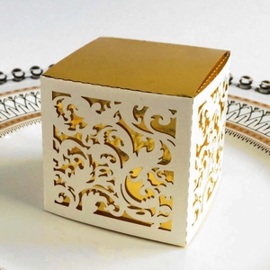 Close-up of laser-cut wedding favor box with ivory filigree and gold metallic liner