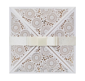 Elegant white laser-cut wedding invitation with intricate floral patterns and cream ribbon bow