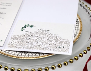 Detailed laser-cut white lace wedding invitation on a luxury dinner plate setting