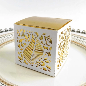 Detail of laser-cut white wedding favor box with elegant gold lining and vine patterns