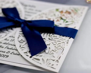 Laser-cut white wedding invitation with a navy blue satin bow and floral pattern