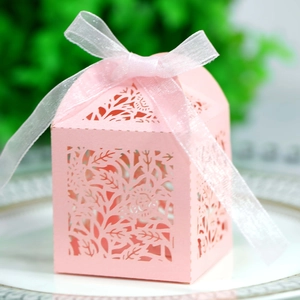Close-up of laser-cut pink wedding favor box with floral patterns and a white ribbon bow