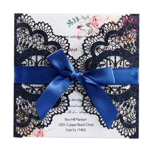 Macro detail of navy blue laser-cut lace invitation with glitter and satin ribbon