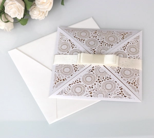 Macro detail of laser-cut white wedding invitation with elegant beige satin ribbon bow