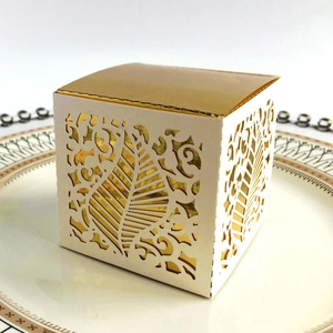 Macro view of white cardstock gift box with laser-cut leaf patterns and golden lining