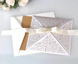 Detail of silver laser-cut floral wedding invitation with kraft insert and ribbon bow