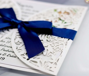 Laser-cut floral wedding invitation with navy blue satin bow and white paper sleeve