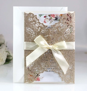 Detail of laser-cut glitter invitation with cream ribbon bow and floral inner card
