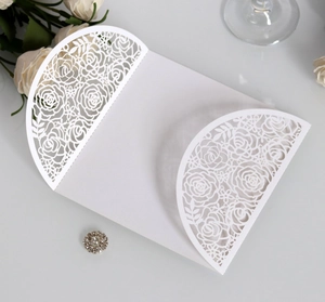 Close-up of laser-cut white rose floral pattern and rhinestone buckle on wedding card