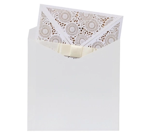 Detail of white laser-cut invitation card with floral patterns and a silk bow