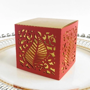 Detail of red and gold wedding favor box with laser-cut vine patterns on a ceramic plate