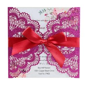 Detail of laser-cut glitter wedding invitation with red ribbon bow and floral insert