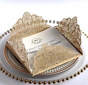 Close-up of laser-cut wedding invitation in champagne gold with floral patterns and insert