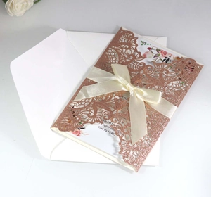 Detailed view of laser-cut rose gold glitter wedding invitation with ivory satin bow