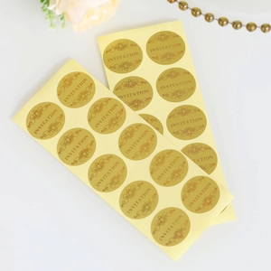 Macro detail of round gold foil invitation stickers with elegant vintage scroll patterns