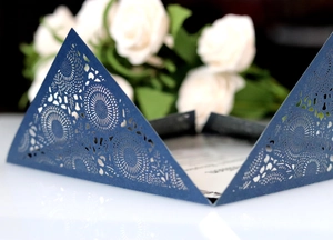 Detail of laser-cut navy blue wedding invitation with intricate floral hollow patterns