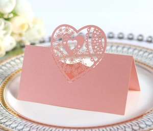 Pink laser-cut heart place card with floral lace design on elegant dinner plate