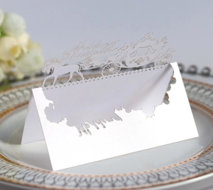 Detail of white laser-cut wedding place card with carriage design on decorative porcelain plate