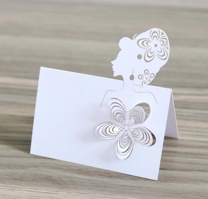 Detailed close-up of a white laser-cut seat card with 3D paper flower on wood background