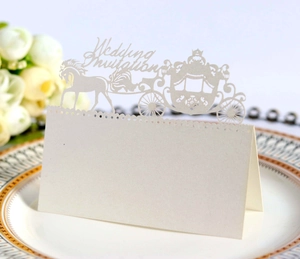 Macro shot of white laser-cut wedding place card with horse carriage and floral details