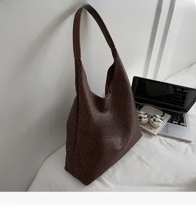Detailed close-up of dark brown woven texture and smooth leather handle on a large hobo tote