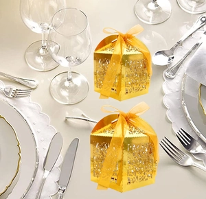 Golden laser-cut wedding candy box with elegant ribbon bow on a dining table setting