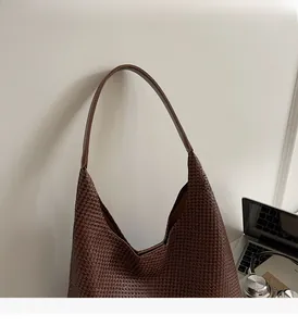 Close-up of dark brown woven tote bag with smooth handles on a minimalist wall background