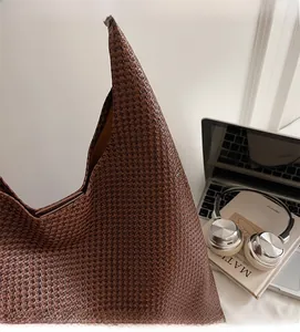 Detail of a brown woven tote bag with Intrecciato pattern next to a laptop and headphones